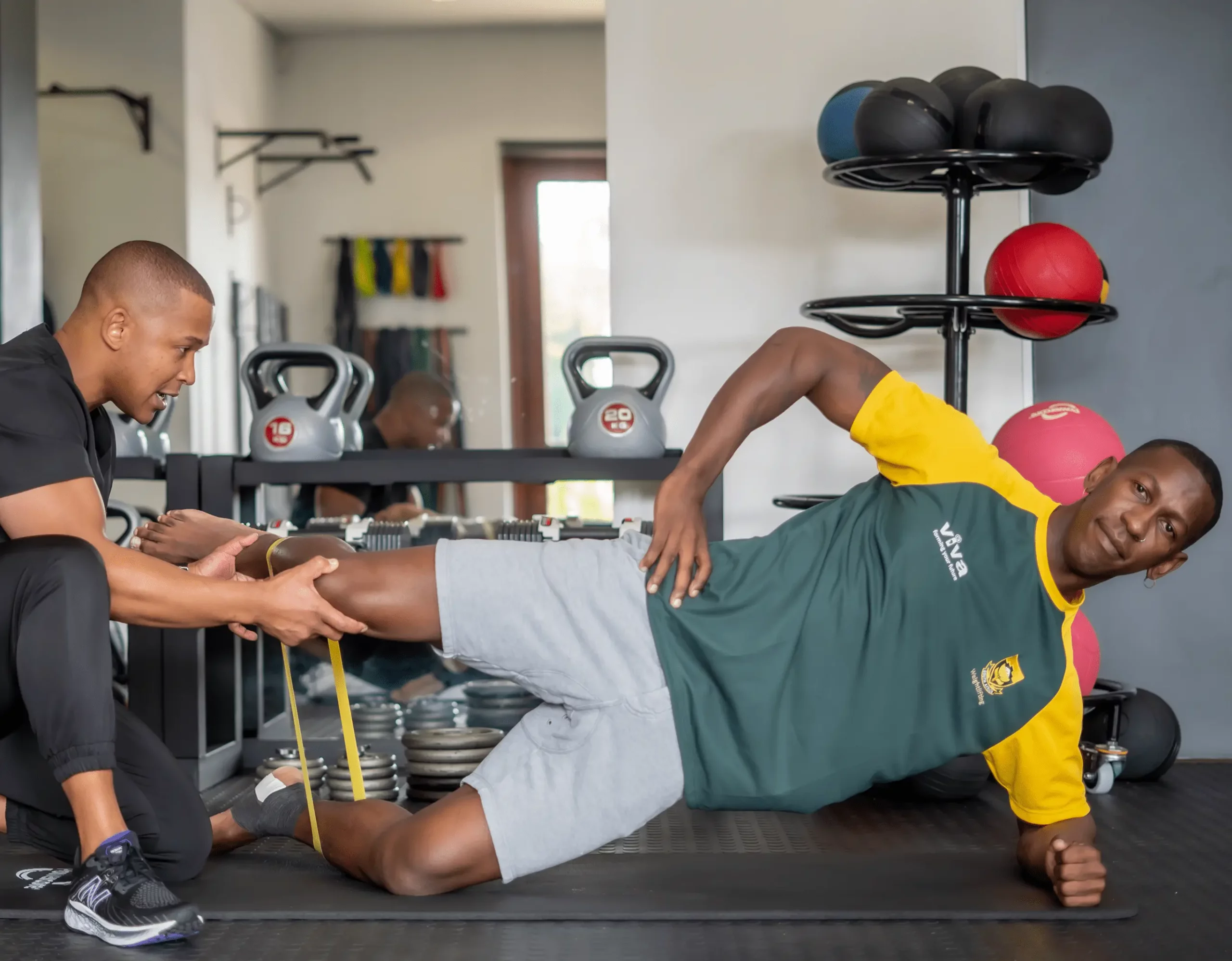 Weightlifting athlete doing side plank with resistance band under physio supervision